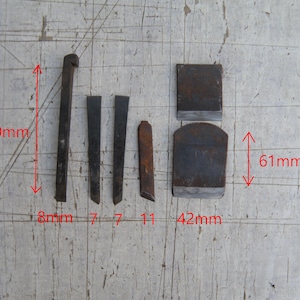 Può includere: Una collezione di sei componenti di utensili in metallo scuro, tra cui quattro barre strette e due piastre piatte. Il testo rosso indica dimensioni di 120mm, 61mm, 42mm, 11mm, 8mm e 7mm. Gli oggetti sono disposti su una superficie chiara incisa.
