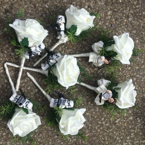 Peut inclure: Ensemble de boutonnières de roses blanches avec des personnages Lego Star Wars attachés. Chaque boutonnière est composée d'une rose blanche, de feuilles vertes et d'une tige argentée.
