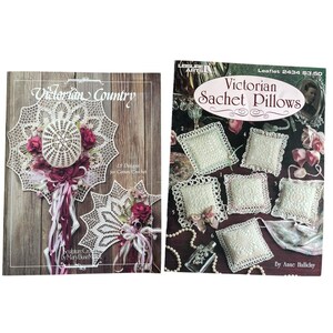 May include: Two vintage crochet pattern books. The first book is titled "Victorian Country" and features a white doily design with red flowers. The second book is titled "Victorian Sachet Pillows" and shows several small, square pillows.