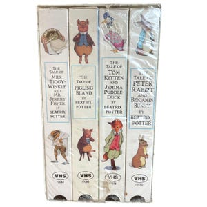 May include: A set of four Beatrix Potter VHS tapes in a white box set. The spines feature illustrations of characters like Peter Rabbit, Pigling Bland, and Jemima Puddle-Duck, with titles including The Tale of Peter Rabbit and Benjamin Bunny.