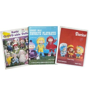 May include: Three instructional craft books featuring crochet dolls on the covers. The left book is titled Kathi GLOVE-able Dolls, the center book is Crochet Dolls FAVORITE PLAYMATES, and the right book is a Darice publication with Heidi Hydrangea, Desert Daisy, and Apple Adam.