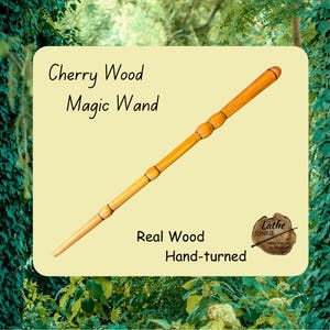 Puede incluir: Una varita mágica de madera de cerezo torneada a mano, con un acabado suave de color marrón claro y detalles de anillos oscuros a lo largo del mango y el eje. El texto en la imagen dice Cherry Wood Magic Wand, Real Wood y Hand-turned.