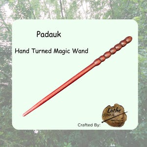 Puede incluir: Una varita mágica de madera de Padauk de color marrón rojizo con un acabado torneado a mano. La varita presenta un eje cónico liso y un mango con seis segmentos redondeados y bulbosos. El texto dice: Padauk, Hand Turned Magic Wand, Crafted By: The Lathe JUNKIE.