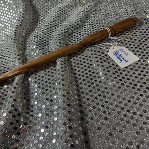 以下が含まれることがあります： 木製の杖。明るい茶色で、テクスチャ加工が施されています。杖はわずかに湾曲しています。小さなタグには「251011 Butternut Company」と書かれています。