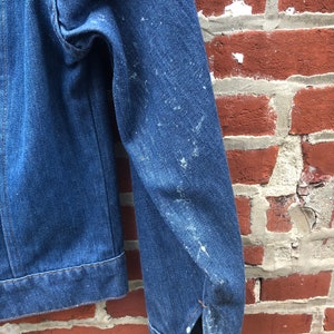 May include: A blue denim jacket with a worn look, showing signs of wear and tear. The jacket has a button closure and a single pocket on the left chest.