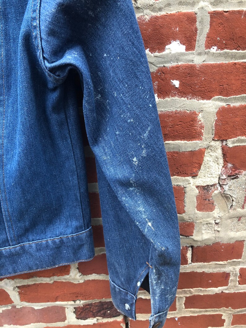 May include: A blue denim jacket with a worn look, showing signs of wear and tear. The jacket has a button closure and a single pocket on the left chest.