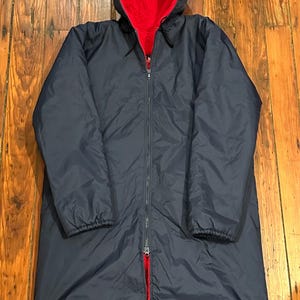 May include: A long navy blue hooded jacket with a red fleece lining. The jacket has a zipper closure and a drawstring hood.