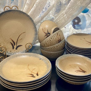 May include: A set of brown and blue ceramic bowls and plates with a subtle floral design. The bowls and plates are stacked and arranged on a black surface.