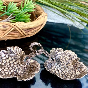 Puede incluir: Dos platos de servir de plata en forma de hoja de vid con un diseño de vid. Los platos están conectados por una vid.