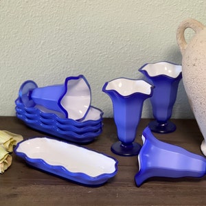 Puede incluir: Conjunto de platos de postre de vidrio azul y blanco con bordes festoneados. El conjunto incluye cuatro platos individuales y un plato rectangular más grande.