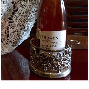 May include: Two bottles of Blason de Bourgogne La Reserve Brut wine in silver metal bottle holders with grapevine designs.