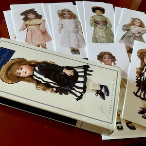 Puede incluir: Un conjunto de ocho tarjetas de mu&ntilde;ecas de estilo vintage que presentan diferentes mu&ntilde;ecas con diversos atuendos. Las tarjetas son blancas con un borde negro y presentan el texto "eighteen card set". Las tarjetas est&aacute;n dispuestas en forma de abanico sobre una superficie roja. Un libro titulado "The Golden Years" se encuentra en primer plano.