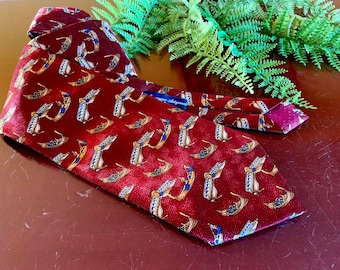 May include: A red silk tie with a repeating pattern of gold and blue gondolas. The tie has a burgundy colored lining and a blue label that reads "Alessandro Delage".