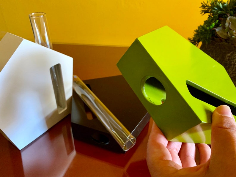 May include: Three geometric shaped planters, one white, one black, and one green. The planters have a slot for a glass tube to hold a plant cutting.