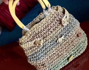 May include: A woven straw handbag with wooden handles and animal-shaped buttons. The bag is a light brown, beige, and green color.