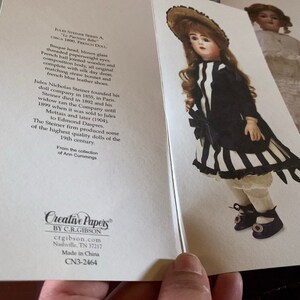 Puede incluir: Una mu&ntilde;eca francesa vintage con cabeza de bisque, ojos de vidrio soplado y vestido a rayas blancas y negras. La mu&ntilde;eca lleva un sombrero de paja y zapatos negros. La tarjeta dice "Jules Nicholas Steiner A. - Le Parisien Body - Circa 1890, French Doll."