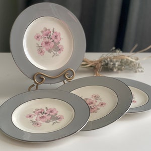 May include: Set of four grey and white ceramic dinner plates with a floral design. The plates have a grey rim and a white centre with pink flowers.