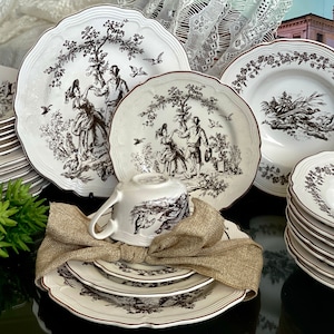Może przedstawiać: Zestaw białej porcelanowej zastawy stołowej z brązowym wzorem kwiatowym. Zestaw zawiera talerze, miski i filiżankę do herbaty.