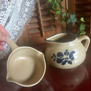 May include: Two ceramic creamers, one with a blue floral design and the other plain, both in a beige color.