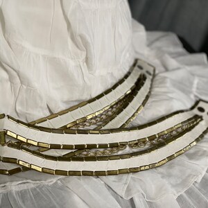 May include: A white leather belt with gold chain accents. The belt is made of multiple strips of leather with gold metal accents.