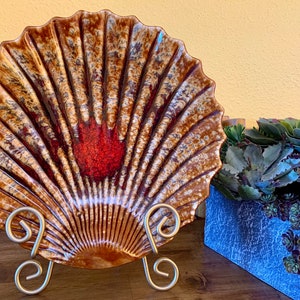 May include: A large, decorative ceramic shell dish with a brown, white, and red glaze. The dish is on a metal stand with three legs.