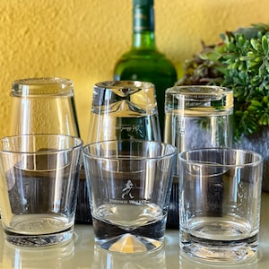 Pu&ograve; includere: Cinque bicchieri di vetro trasparente, quattro dei quali sono su una superficie marrone scuro. Uno dei bicchieri ha il logo Johnnie Walker stampato sul fondo.