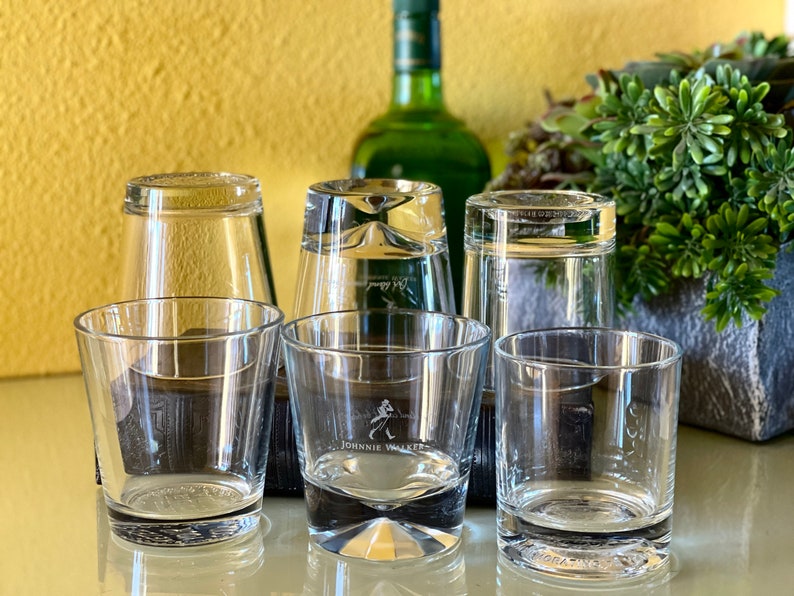 Pu&ograve; includere: Cinque bicchieri di vetro trasparente, quattro dei quali sono su una superficie marrone scuro. Uno dei bicchieri ha il logo Johnnie Walker stampato sul fondo.