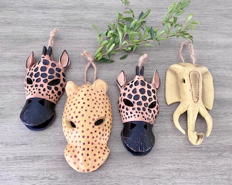 May include: Four wooden animal masks with black and brown spots and a yellow elephant mask. The masks are hanging from twine.