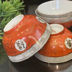 May include: Four orange and white ceramic bowls with gold accents and Chinese characters. The bowls have a decorative pattern of flowers and a geometric border.