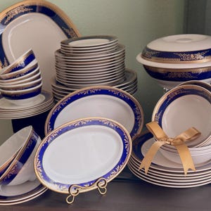 May include: A set of blue and gold rimmed dinnerware with a floral design. The set includes plates, bowls, and serving dishes.