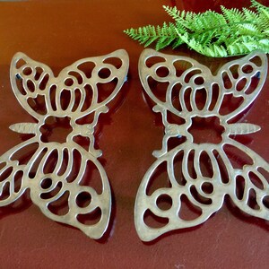 May include: Two silver butterfly-shaped trivets. The trivets are made of a delicate, openwork design and are perfect for protecting surfaces from hot dishes.