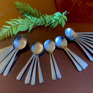 Op de afbeelding: Een set van 10 zilveren theelepels, gerangschikt in een waaier op een bruin oppervlak. De lepels zijn allemaal even groot en even gevormd, en ze hebben een eenvoudig, elegant ontwerp.
