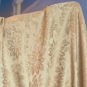 May include: A cream-colored fabric with a raised embossed pattern of poinsettia flowers and holly leaves.