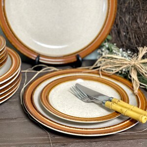May include: A set of brown and white ceramic dinner plates with a brown rim. The plates are stacked on top of each other. There are two forks and a knife with yellow bamboo handles on top of the plates.