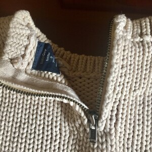 May include: A cream-colored knitted sweater with a zipper closure. The sweater has a label that reads "babyGap toddler 3 years".