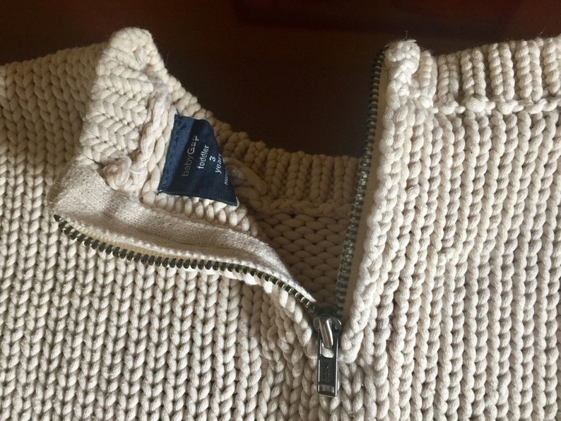 May include: A cream-colored knitted sweater with a zipper closure. The sweater has a label that reads "babyGap toddler 3 years".