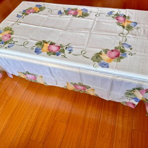 May include: White tablecloth with a floral design featuring fruit and leaves. The design is in shades of green, yellow, pink, and blue.