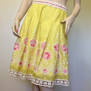 May include: A yellow cotton skirt with pink and white floral embroidery and a white crochet trim.