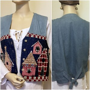 May include: A blue denim vest with a quilted panel featuring a winter scene with houses, trees, and birds. The vest has a tie closure at the back.