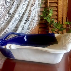 May include: A white and blue ceramic baking dish with two handles. The dish has a blue rim and a white interior.