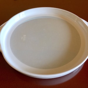 Może przedstawiać: Biała ceramiczna forma do pieczenia o gładkiej, lekko fakturowanej powierzchni. Forma ma zaokrąglony owalny kształt z dwoma małymi uchwytami po bokach.