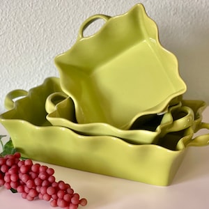 May include: Set of three green ceramic baking dishes with scalloped edges and handles. The dishes are stacked on top of each other.