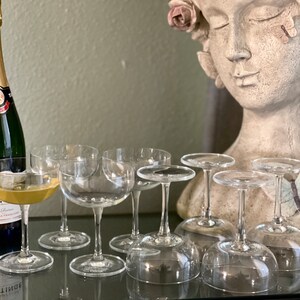May include: A set of eight clear glass champagne coupes, some filled with a pale yellow liquid, with a bottle of Taittinger Brut La Francaise champagne in the background.