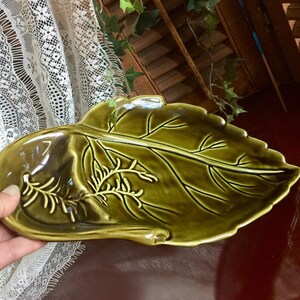 May include: A green ceramic serving dish shaped like a leaf with a raised design. The dish has a deep center section and two smaller side sections.