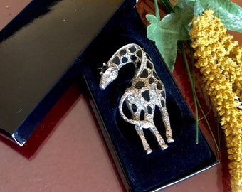 May include: A silver giraffe brooch with black enamel spots, set in a black velvet box. The brooch is detailed with sparkling rhinestones.