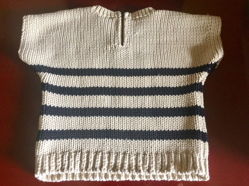 May include: A beige and black striped knitted sweater with short sleeves and a zipper at the back of the neck.