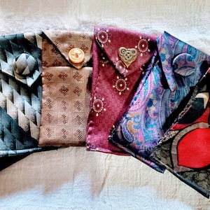 May include: Six small fabric pouches made from repurposed ties. The pouches are in various colors and patterns, including green, brown, red, and purple. Each pouch has a button closure and a unique design.