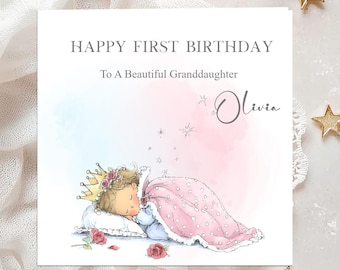 May include: A greeting card with the text "Happy First Birthday To A Beautiful Granddaughter Olivia." The card features an illustration of a sleeping child wearing a crown and covered with a pink blanket. Roses and stars are also depicted.