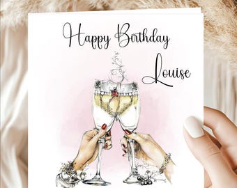May include: A greeting card with the words "Happy Birthday Louise" in elegant script. The illustration features two champagne flutes clinking, held by hands with red nail polish, against a pink background.