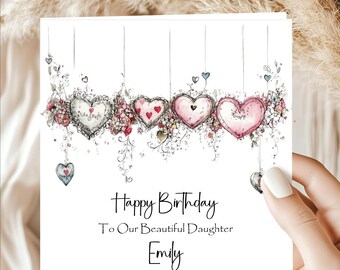 May include: A white birthday card with the text "Happy Birthday To Our Beautiful Daughter Emily." The card features watercolor hearts with floral accents. The hearts are in shades of pink and white, with hanging heart details.